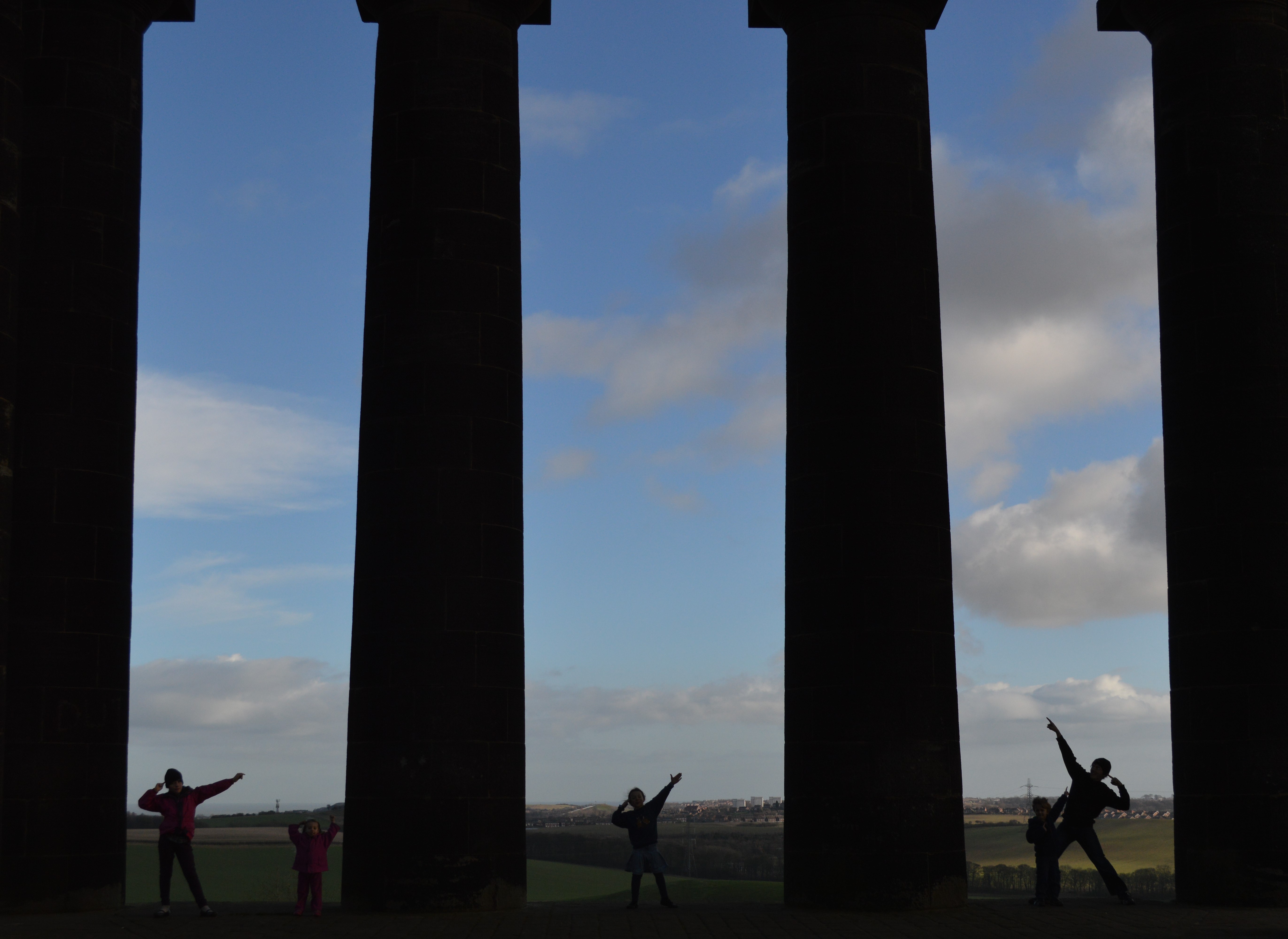 5 people between pillars sihouetted on a landscape